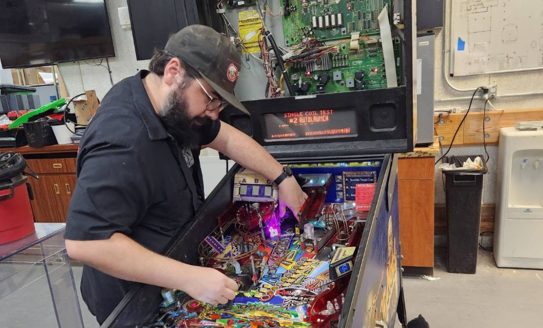 Starrcade technician servicing a pinball machine playfield in the workshop